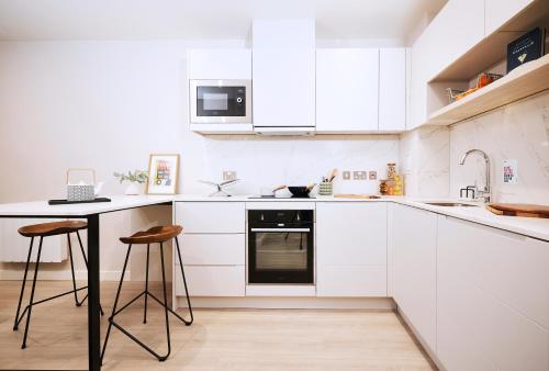 a kitchen with white cabinets and a table and stools at JOIVY at Vita Iona Street - Adults only in Edinburgh