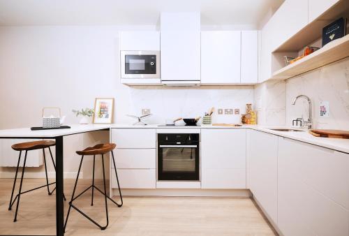 a kitchen with white cabinets and a table and stools at ALTIDO Aparthotel at Vita Iona Street - Adults only in Edinburgh