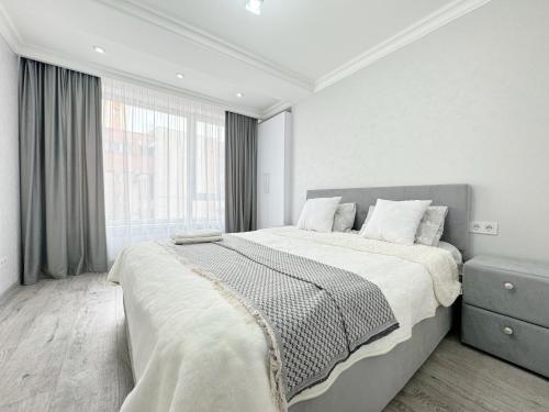 a white bedroom with a large bed and a window at Bella White Apartment in Chişinău