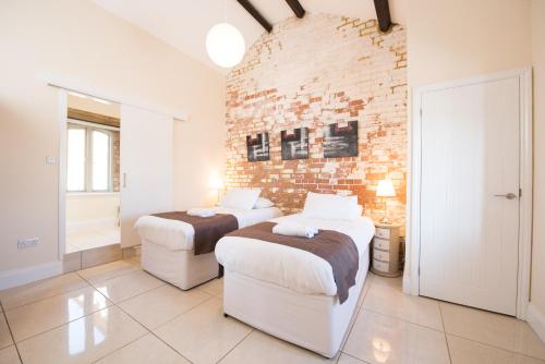 a bedroom with two beds and a brick wall at Weasels Way at Tove Valley Cottages in Towcester