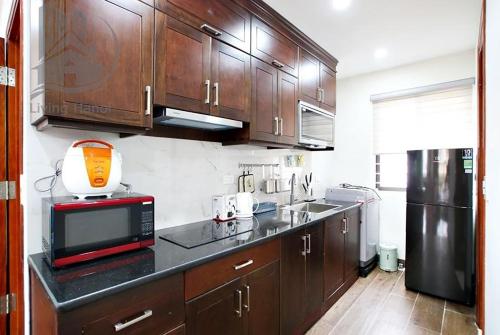 La cuisine est équipée de placards en bois, d'un four micro-ondes et d'un réfrigérateur. dans l'établissement Splendor Trendy Aparment, à Hanoï