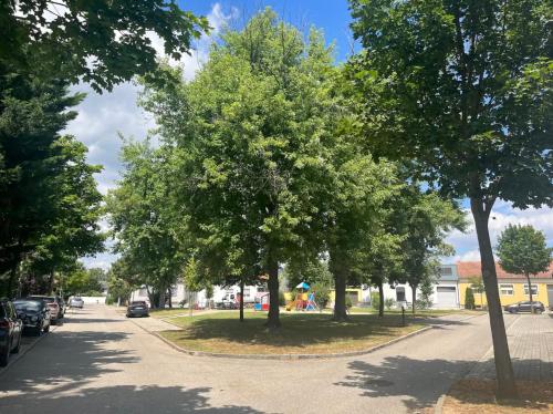 een met bomen omzoomde straat met een park met een speeltuin bij Haus Im Park in Neusiedl am See