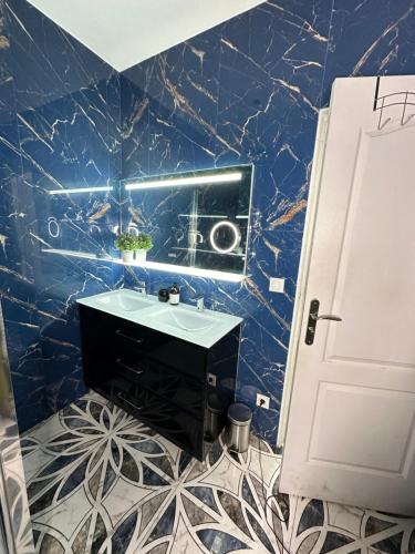 een blauw betegelde badkamer met een wastafel en een spiegel bij Chambre cozy proche Paris/CDG in Le Blanc-Mesnil