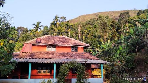 an orange house with a roof in front of a mountain at Kyathanamakki Base Camp Stay in Kalasa