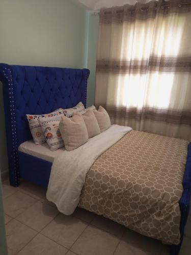 a bed with a blue headboard and pillows on it at Verona Apartments in Thika