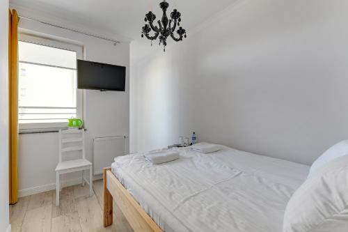 a white bedroom with a bed and a chandelier at Grobla Centre 4 by Grand Apartments in Gdańsk