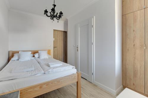 a bedroom with a bed with white sheets and a chandelier at Grobla Centre 4 by Grand Apartments in Gdańsk
