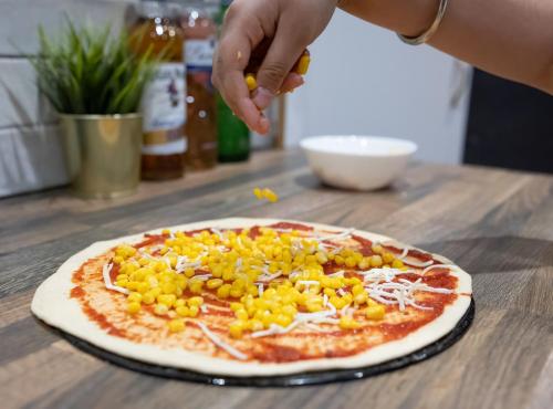 a person sprinkling corn on a pizza on a table at County Hotel in Helensburgh