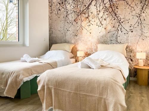 two beds in a room with a wall with branches at PEARLs - Stilvolle Neubauwohnung am Niederrhein in Elten