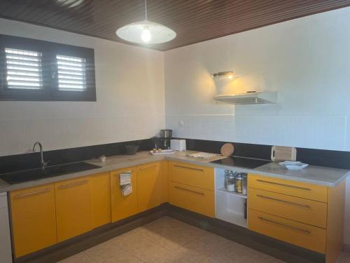 una cocina con armarios amarillos y fregadero en Villa Ressources, paisible et avec vue dégagée, en Rivière-Salée