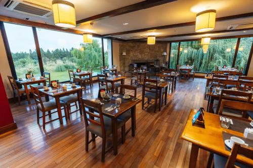 un restaurante con mesas y sillas de madera y ventanas grandes en Loi Suites Chapelco Hotel en San Martín de los Andes