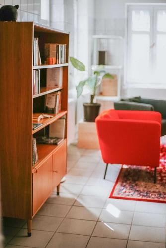 a living room with a red chair and a book shelf at BIG MAMA Leipzig in Leipzig