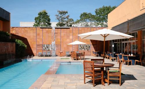 a pool with tables and chairs and an umbrella at Carlton Plaza Baobá in Taubaté