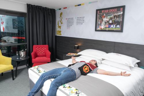 a man laying on a bed with a pizza at Hotel Football, Old Trafford, a Tribute Portfolio Hotel in Manchester