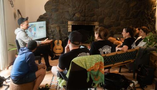 um grupo de pessoas sentadas em uma sala de estar assistindo a uma apresentação em Aldeia Caiçara Surf House em Sagres