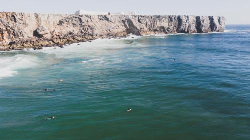 people swimming in the water near a rocky beach at Aldeia Caiçara Surf House in Sagres