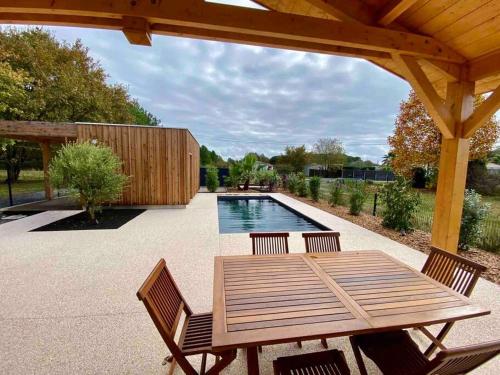 een patio met een houten tafel en stoelen en een zwembad bij Magnifique maison proche lac avec piscine chauffée in Sanguinet