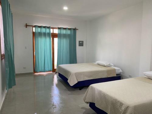 1 dormitorio con 2 camas y una ventana con cortinas azules en Penguin House, en Puerto Villamil