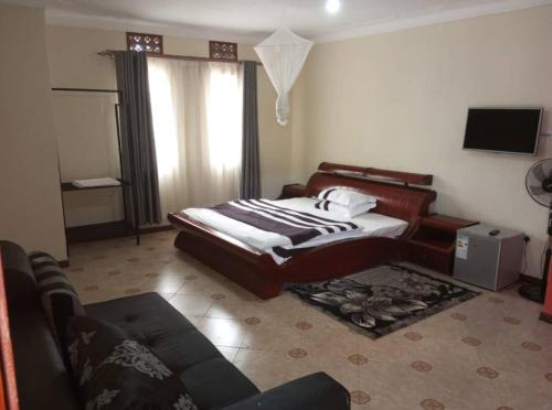 1 dormitorio con cama, sofá y TV en Migingo Suites en Entebbe