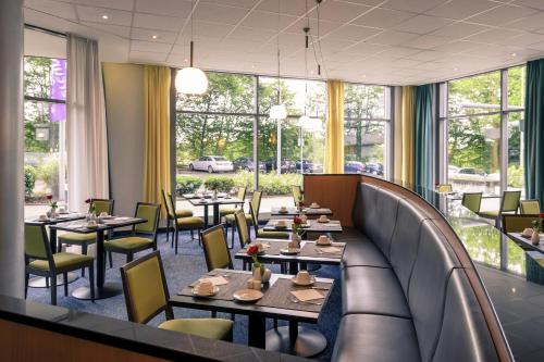 a restaurant with tables and chairs and windows at Mercure Hotel Frankfurt Eschborn Süd in Eschborn