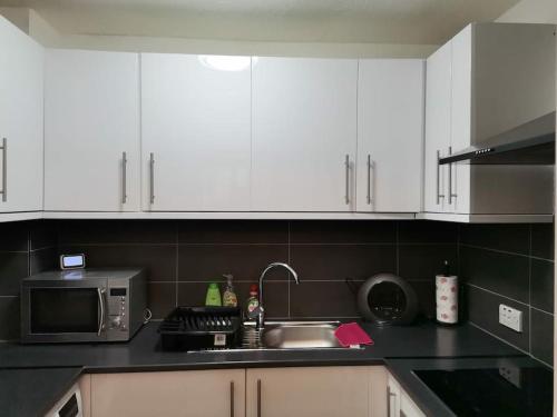 a kitchen with white cabinets and a sink and a microwave at Newly Renovated Cosy 1 bed flat, 4 minutes walk to Town Centre, 3 minutes walk to the train station, Free parking, Modern, fresh and spacious living room, Netflix ready smart TV, Wifi in Wellingborough