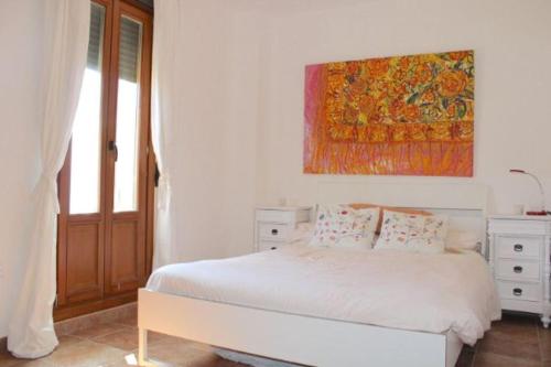 a white bedroom with a bed and a painting on the wall at ACOGEDOR ADOSADO DE ESQUINA. LAS LOMAS. JUNTO AL ALGARVE PORTUGUÉS. in Huelva