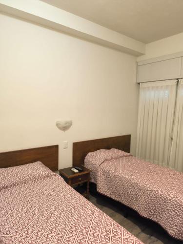 a bedroom with two beds and a nightstand between them at Hotel Lobato in Paysandú