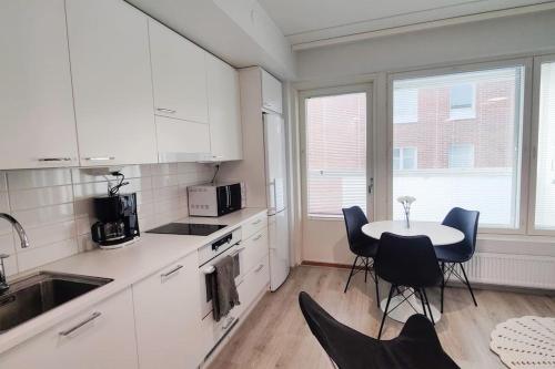 cocina con armarios blancos, mesa y sillas en Lovely new studio for 3 - close to airport, free parking, en Vantaa