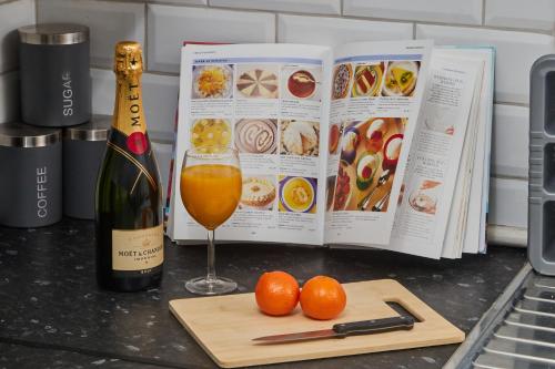 a book and a glass of wine and oranges on a counter at NEW! Perfect for Families & Corporates - 3 Beds - Contact us for Better Offers! in Leeds
