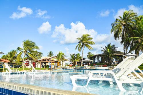 un complejo con piscina con sillas blancas en el agua en Pousada Paradise, en Coruripe