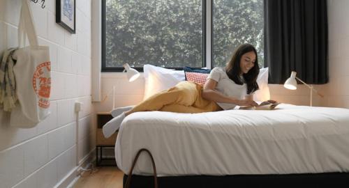 Una donna seduta su un letto che legge un libro di The Village Bondi Beach a Sydney