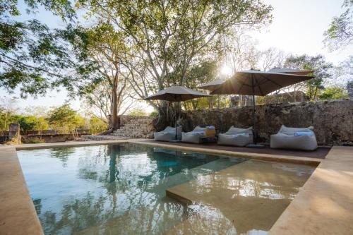 a swimming pool with umbrellas and pillows next to a wall at Viatura Hacienda Xtojil, Yucatan, Merida, with Optional All Inclusive in Sotuta de Peón