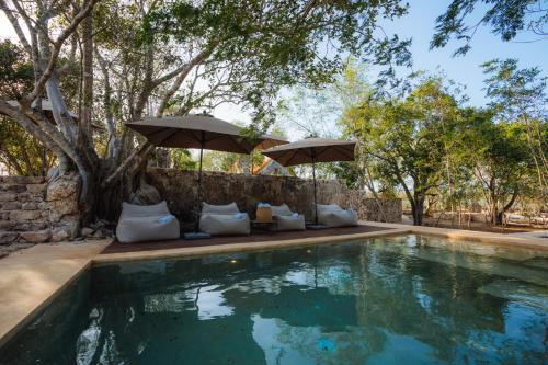 a swimming pool with two umbrellas and pillows next to at Viatura Hacienda Xtojil, Yucatan, Merida, All Inclusive 