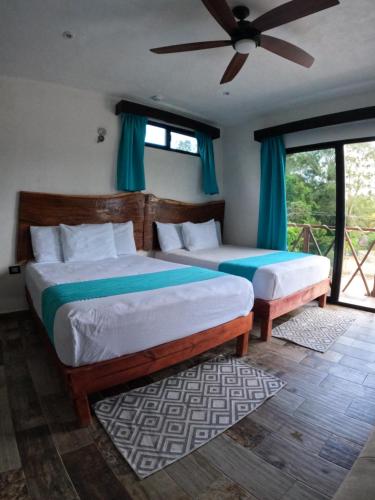 a bedroom with two beds with blue curtains and a fan at Hotel y Beach Club Casa Mia Xulha -Bacalar in Xul-Ha