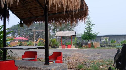 a group of red chairs under a straw umbrella at เช็คอินรีสอร์ทชัยนาท Check-in resort in Ban Khao Khayai (1)