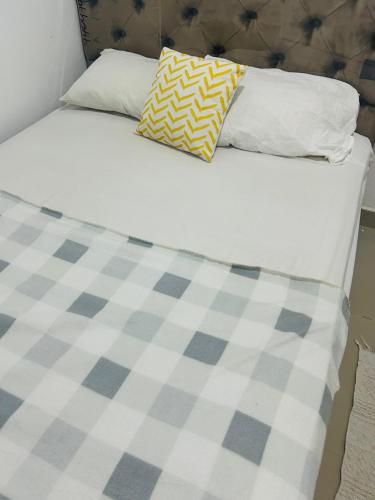a bed with white sheets and a yellow and white pillow at Mini departamento in Pucallpa