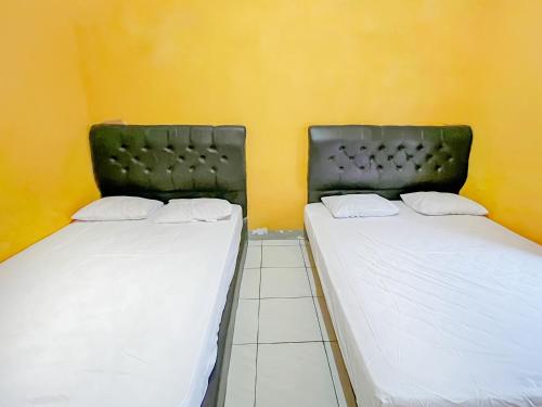 two beds in a room with yellow walls at Penginapan Diar near Pantai Santolo Mitra RedDoorz in Cilauteureun