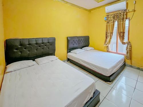 two beds in a room with yellow walls at Penginapan Diar near Pantai Santolo Mitra RedDoorz in Cilauteureun