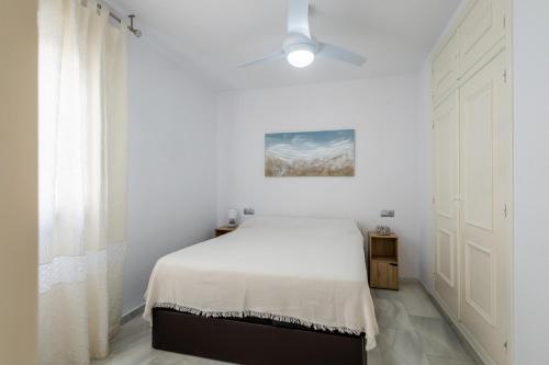 um quarto branco com uma cama e uma ventoinha de tecto em Piso de playa con piscinas em Motril