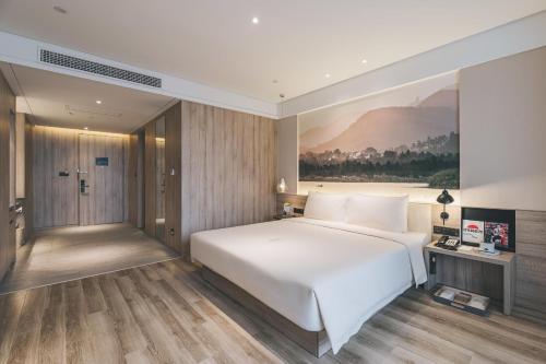 南京市にあるAtour Hotel Nanjing South Stationの白いベッドと壁に絵画が飾られたベッドルーム1室