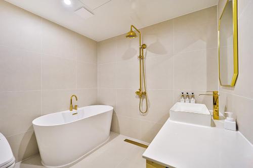 a white bathroom with a tub and a sink at Denbasta Hotel Daeyeon in Busan