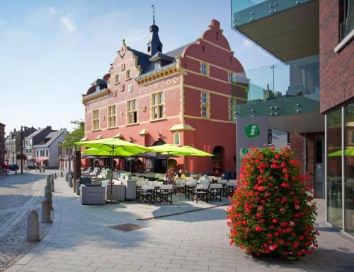 a building with tables and umbrellas on a city street at Hotel De Boskar Peer in Peer