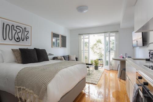 a white bedroom with a large bed and a kitchen at Boutique Studio Apartment in Heritage Home in Sydney