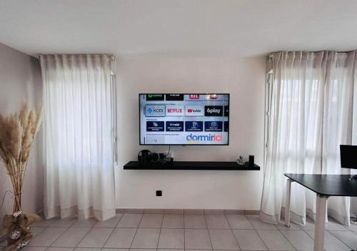 - un salon avec une télévision sur un mur pourvu de rideaux dans l'établissement Lormont City, proche Bordeaux, piscine et parking, à Lormont