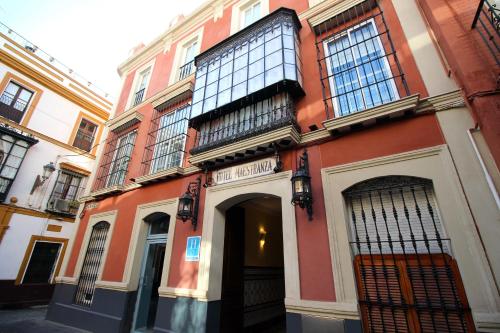 a red and white building with a door and a balcony at Hotel Maestranza in Seville