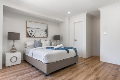 a bedroom with a bed with white walls and wooden floors at Coastal Charm: Halls Head Getaway in Mandurah in Mandurah