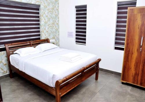 um quarto com uma cama de madeira e lençóis brancos em Whiteway Homestay em Kūmudi