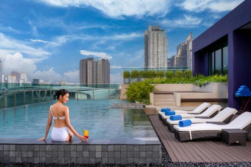 Eine Frau im Bikini steht neben einem Pool. in der Unterkunft Mercure Bangkok Makkasan in Bangkok