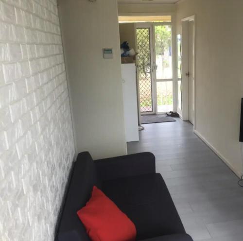 ein Wohnzimmer mit einem schwarzen Sofa und einem roten Kissen in der Unterkunft Private Room in a Shared House-Close to City & ANU-4 in Canberra