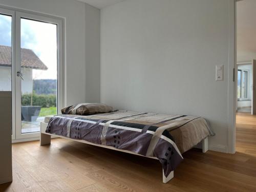 Bett in einem weißen Zimmer mit einem großen Fenster in der Unterkunft Gartenwohnung im modernen Stil in Unterkulm